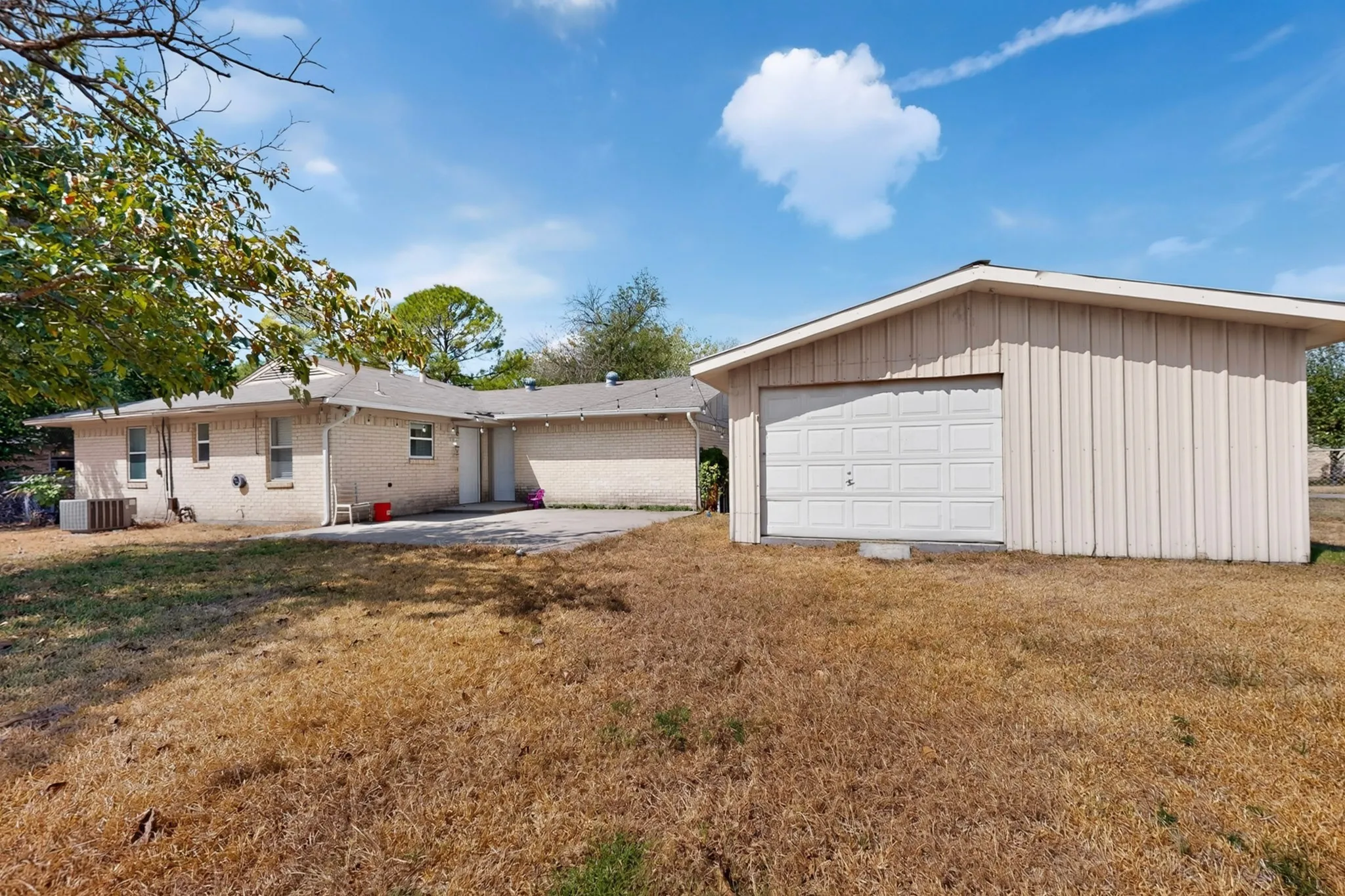 Detached garage with a paneled door, brick exterior, and concrete patio