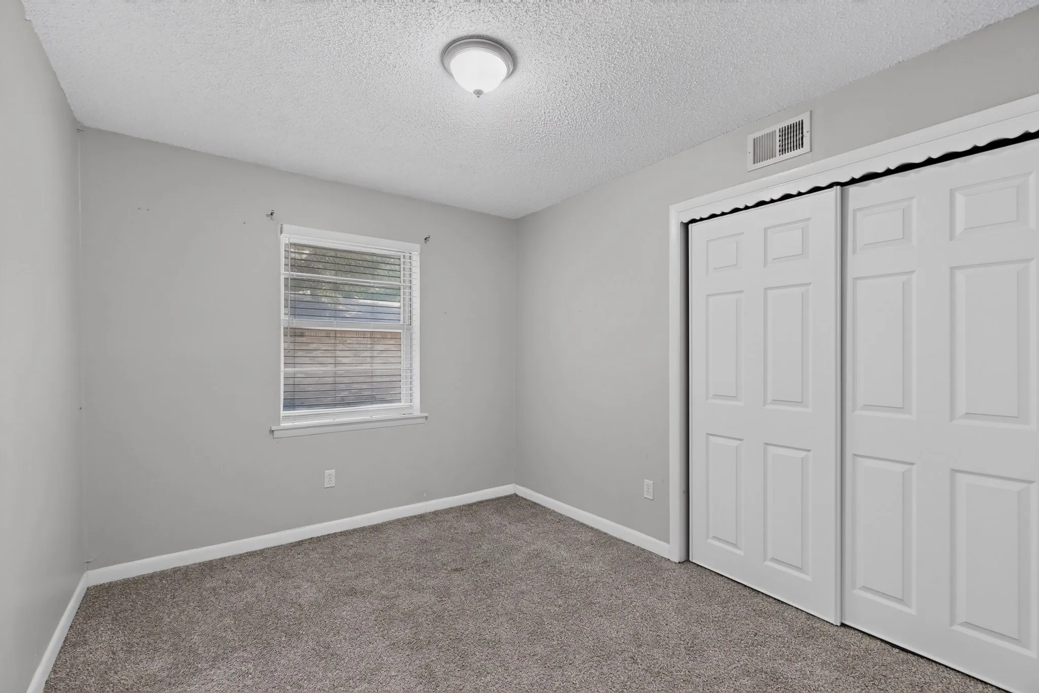 Carpeted flooring, window with blinds, ceiling-mounted light fixture, and white bi-fold closet doors