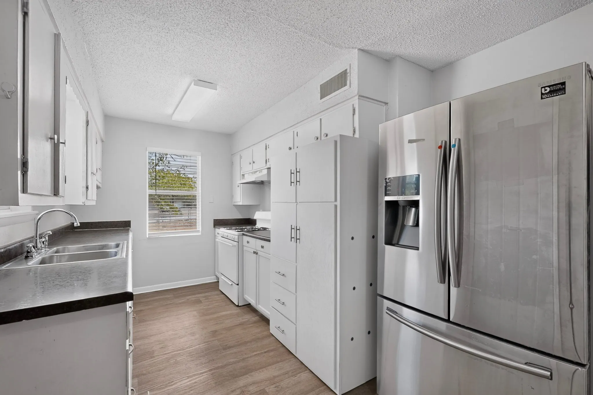 Kitchen featuring wood-finish flooring, white cabinetry, a double-basin stainless steel sink, and stainless steel appliances