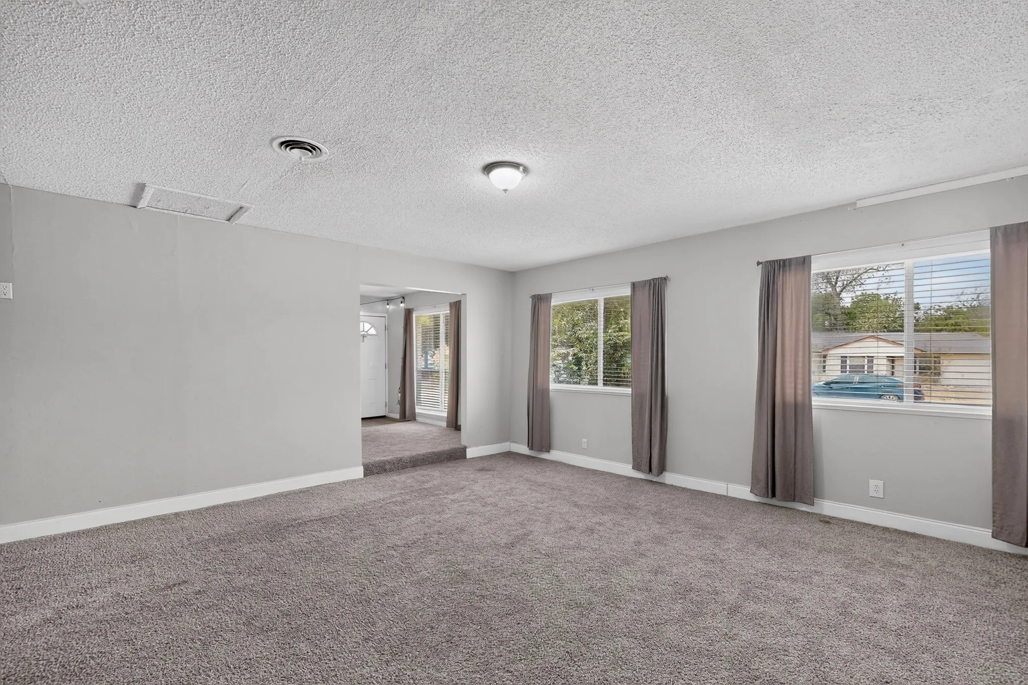 Spacious room featuring neutral carpet, light gray wall paint, and multiple windows