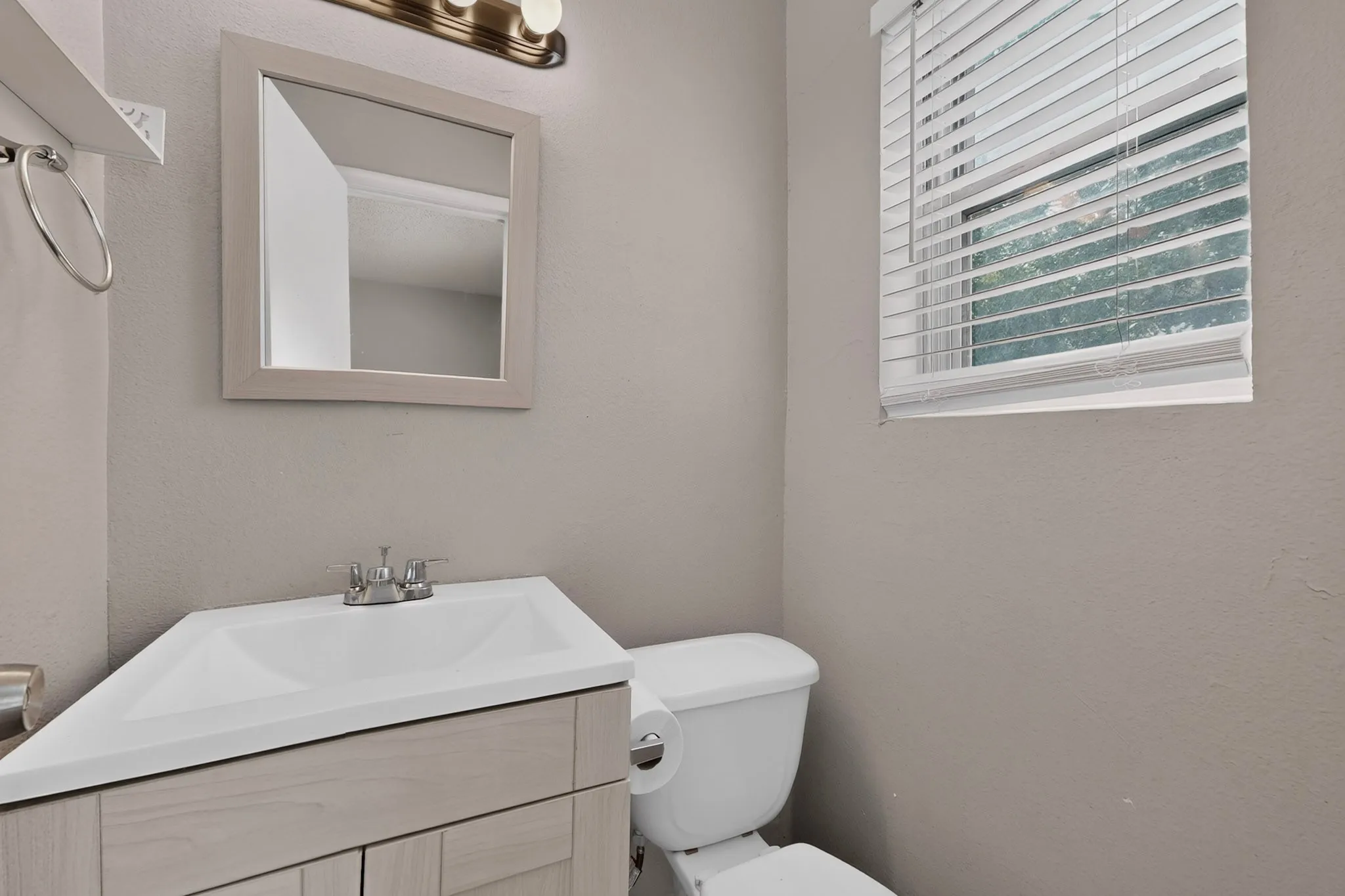 Bathroom featuring a corner vanity with an integrated sink, dual-handle faucet, framed mirror, and window with blinds