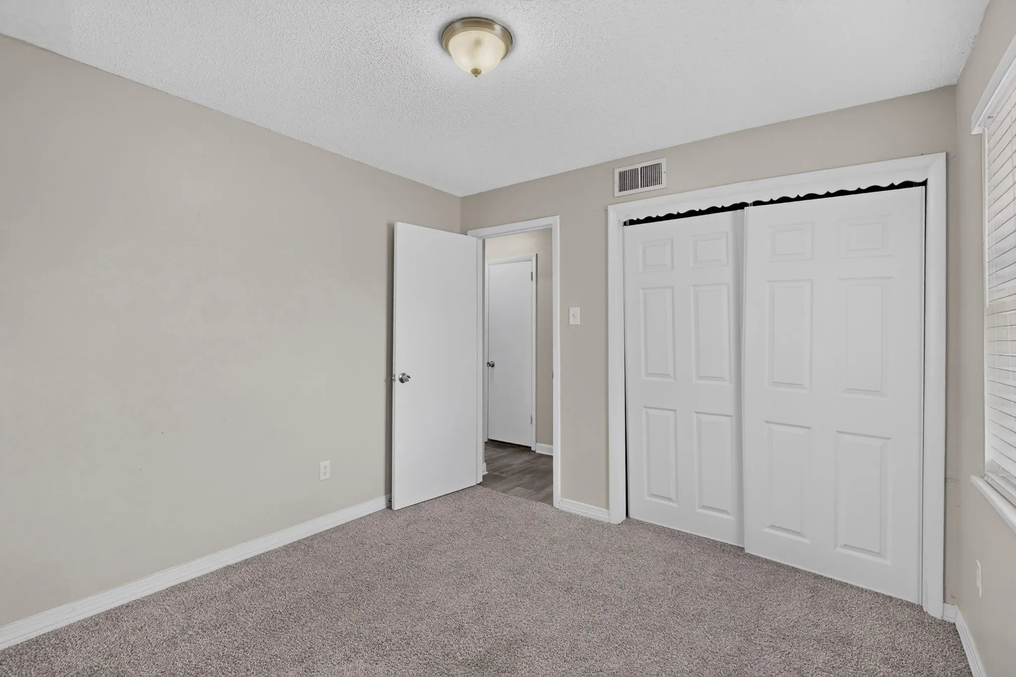Neutral wall paint, carpet flooring, flush mount ceiling light, white paneled bi-fold closet doors, and white window blinds