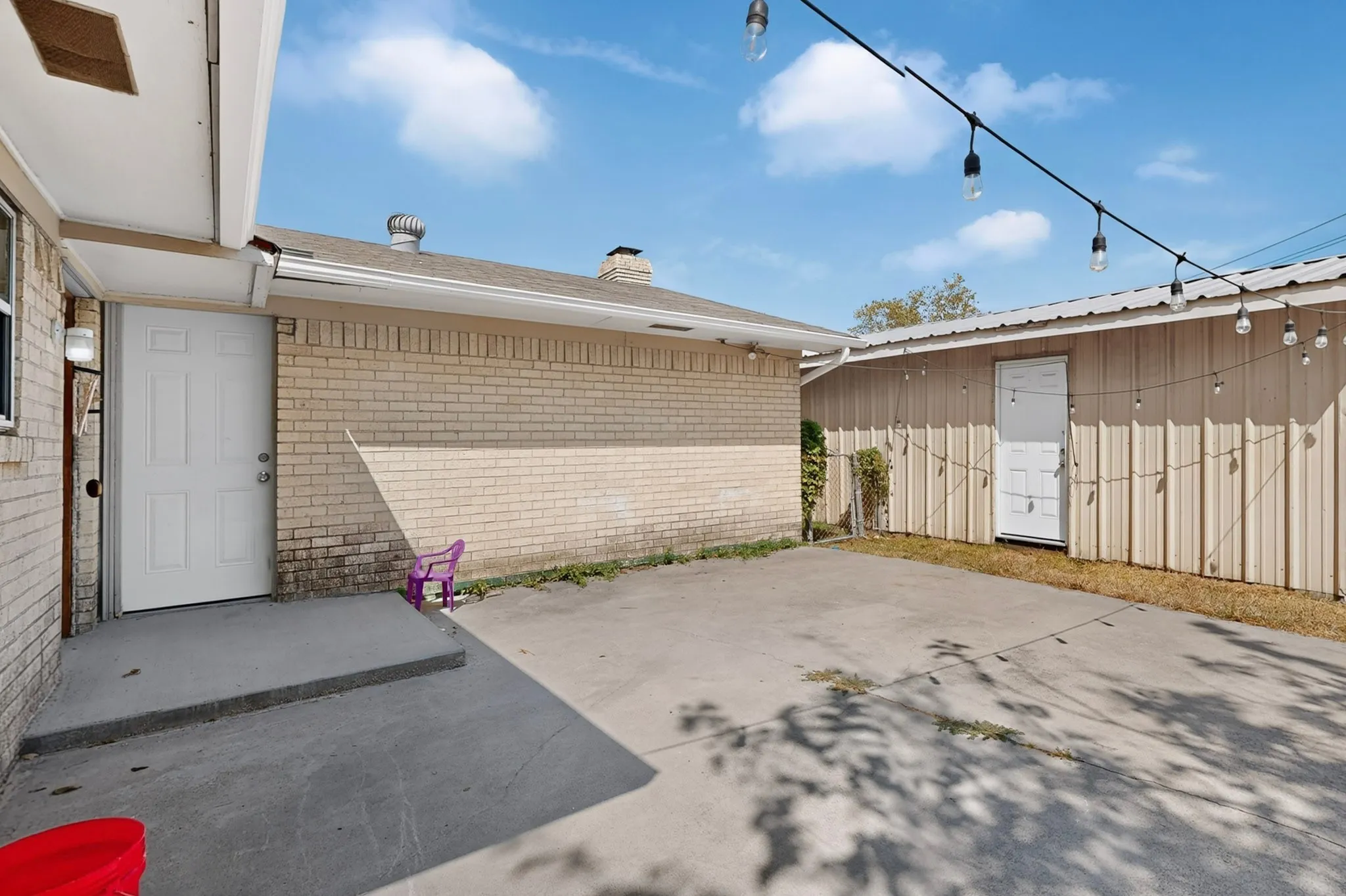 Concrete patio area with a brick exterior and a utility building featuring string lighting