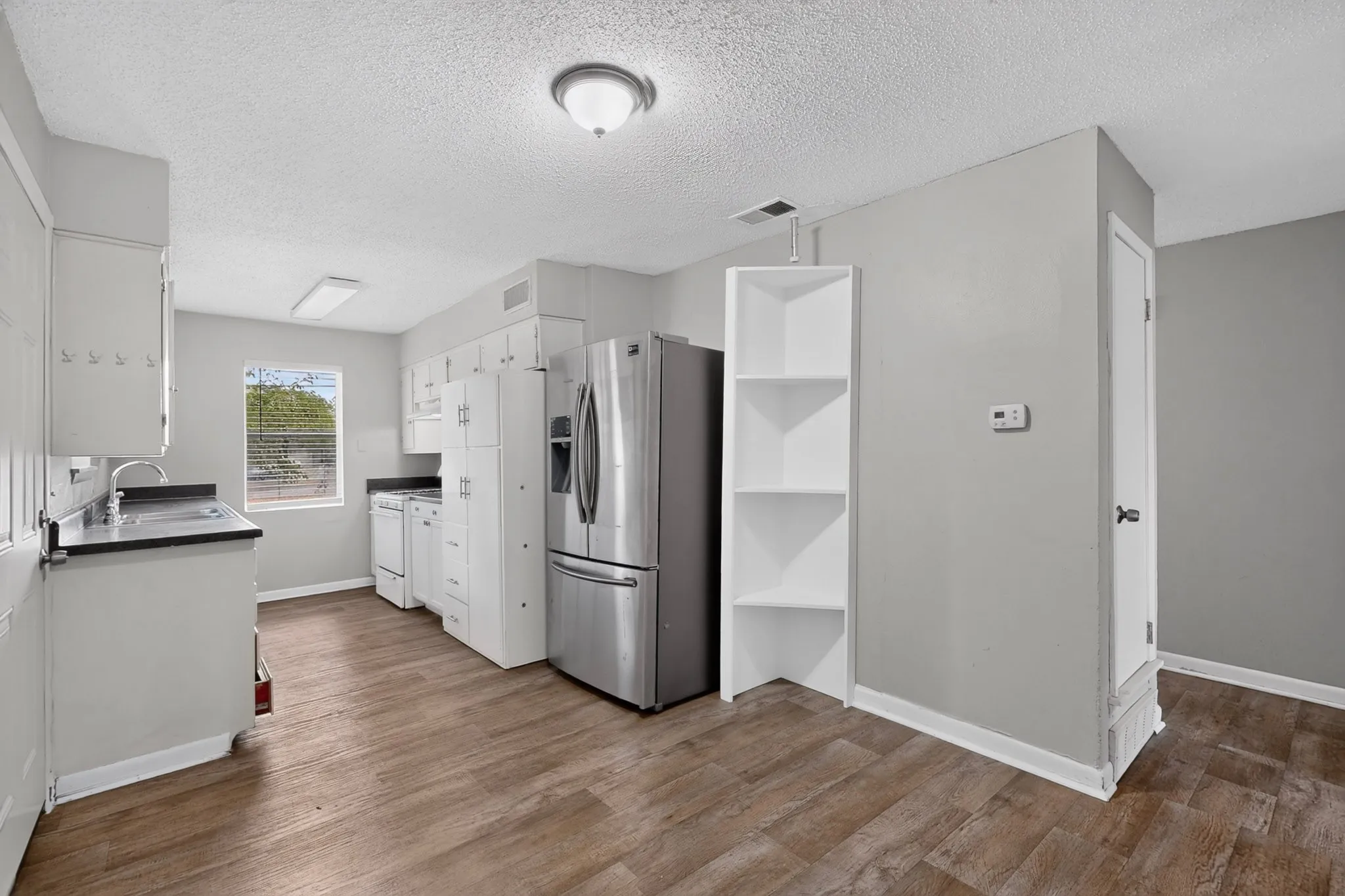 Kitchen featuring white cabinetry, dark countertops, a stainless steel refrigerator, and wood-finish flooring