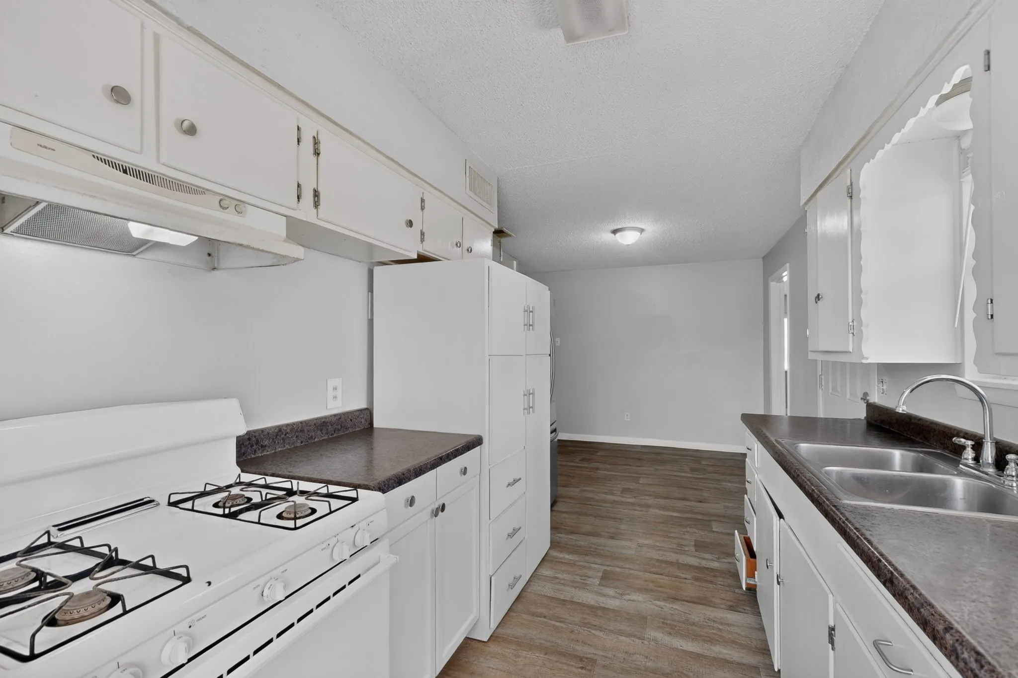 Kitchen featuring white cabinetry, dark countertops, a gas range with an overhead hood, and a double basin sink