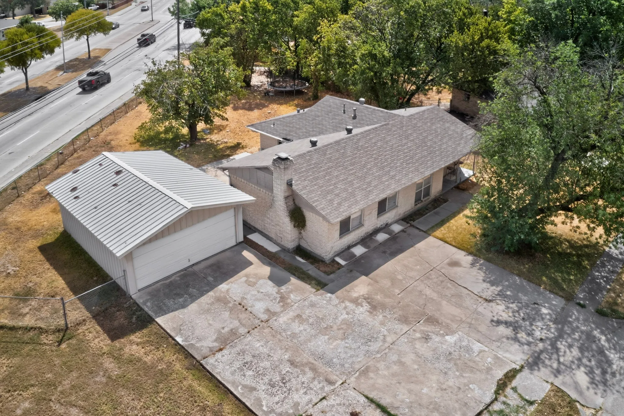 Stone exterior, asphalt shingle roofing, detached metal roof garage, concrete driveway, and mature trees
