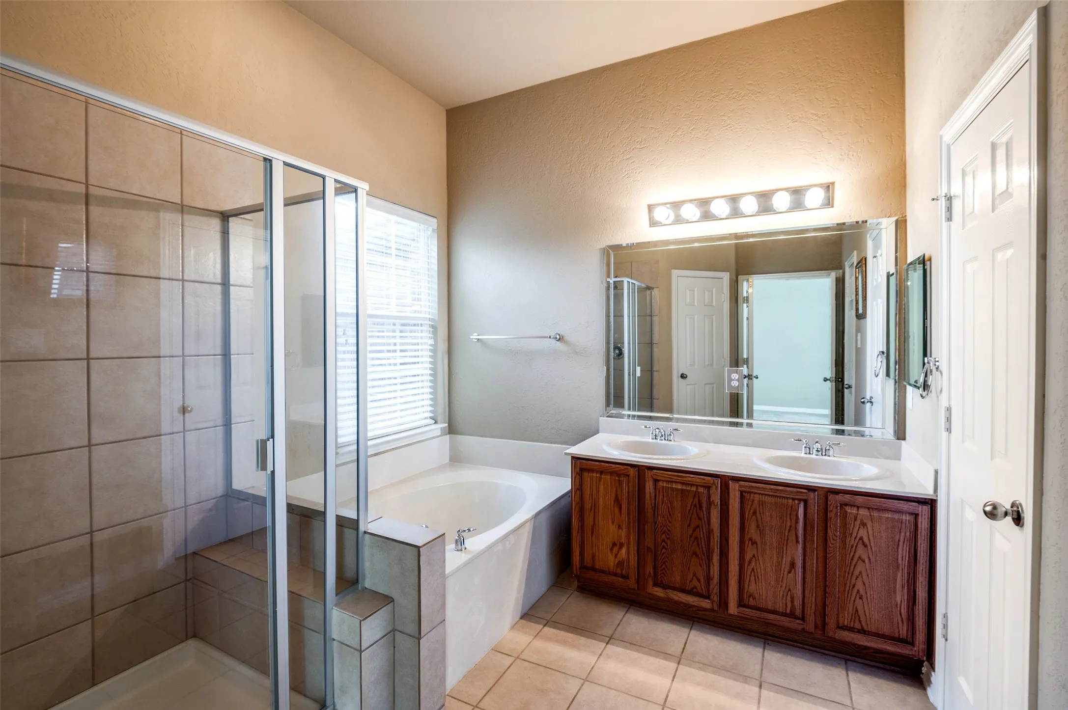 Spacious bathroom featuring a dual vanity with wood-finish cabinetry, a large framed mirror, and an adjacent shower with a built-in bench