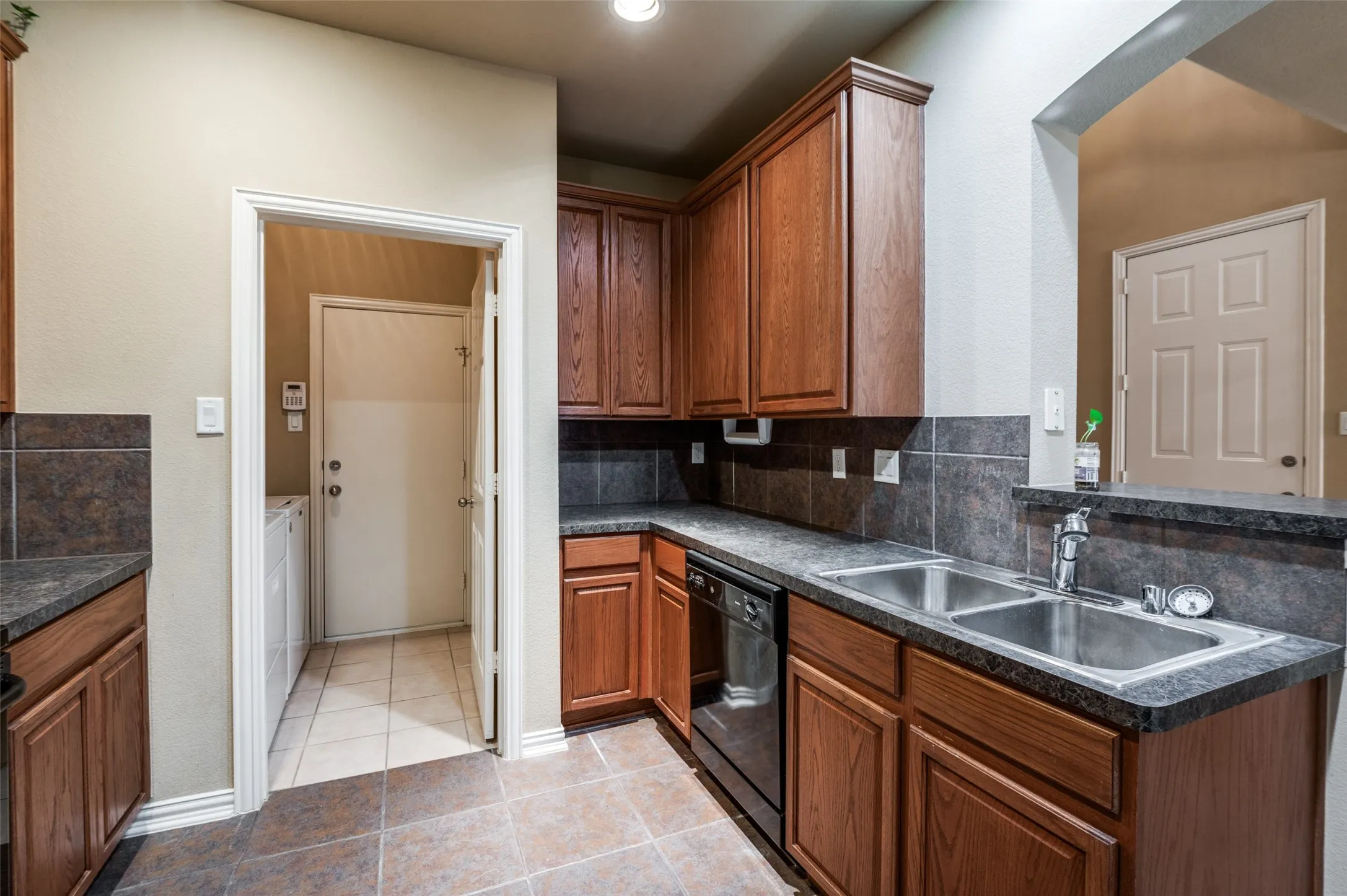 Kitchen featuring wood cabinetry, stone-look countertops, a double basin stainless steel sink, and a tile backsplash