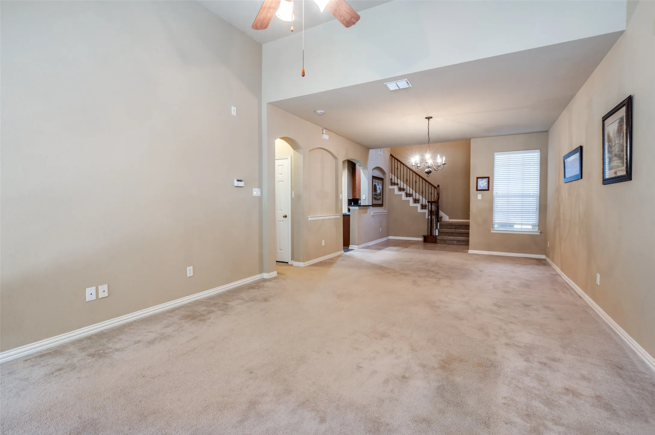 Vaulted ceilings, a ceiling fan, arched doorways, a chandelier, and a wood staircase with balusters
