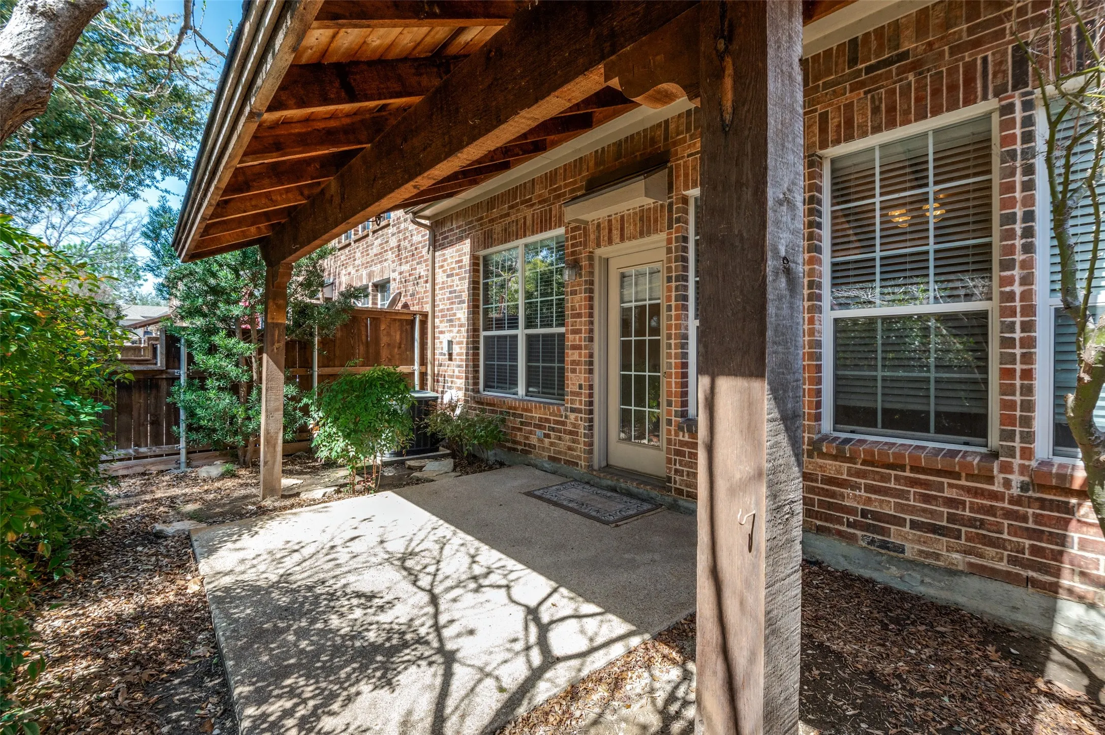 Brick exterior with covered concrete patio, wood-finish ceiling, and multiple windows