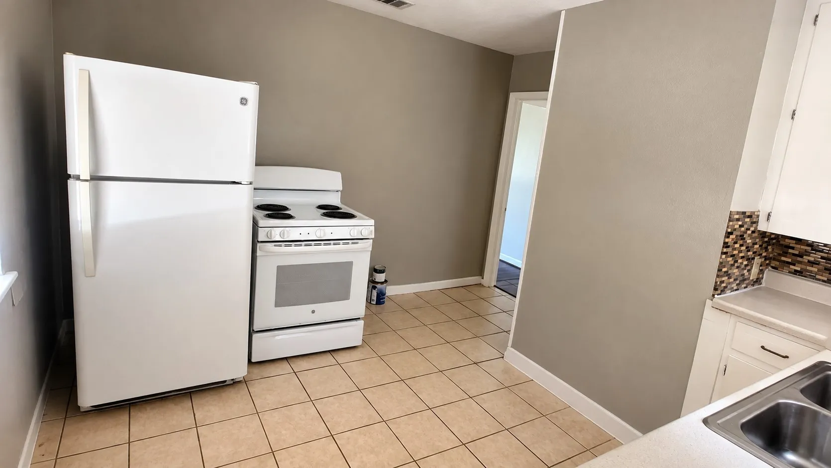 Kitchen featuring tile flooring, white cabinetry, a dual basin stainless steel sink, and a mosaic tile backsplash