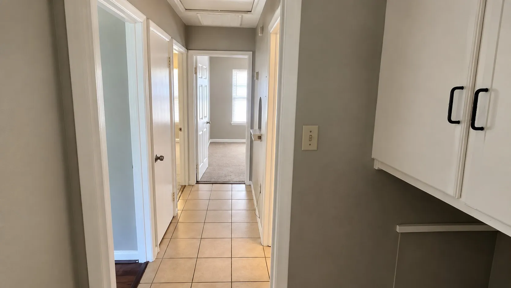 Hallway featuring tile flooring, painted walls, white trim, and built-in white cabinetry with dark pull handles