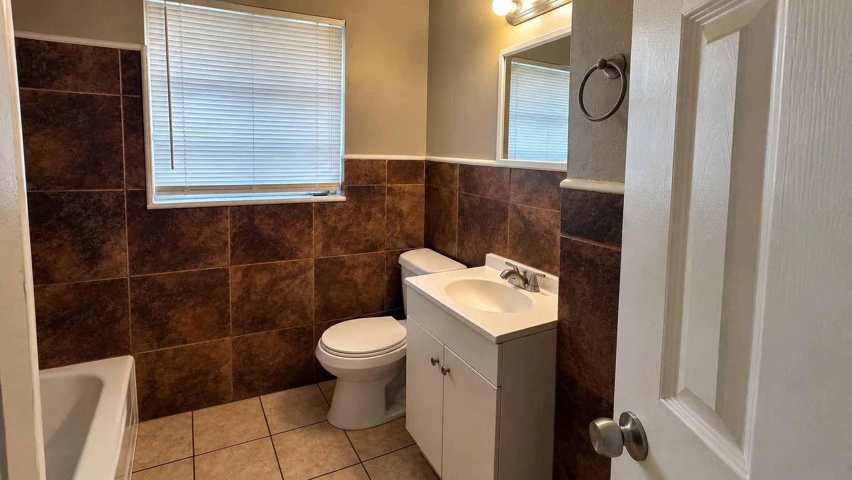 Full bathroom featuring a single vanity, a toilet, a bathtub, and brown-toned tile wainscoting