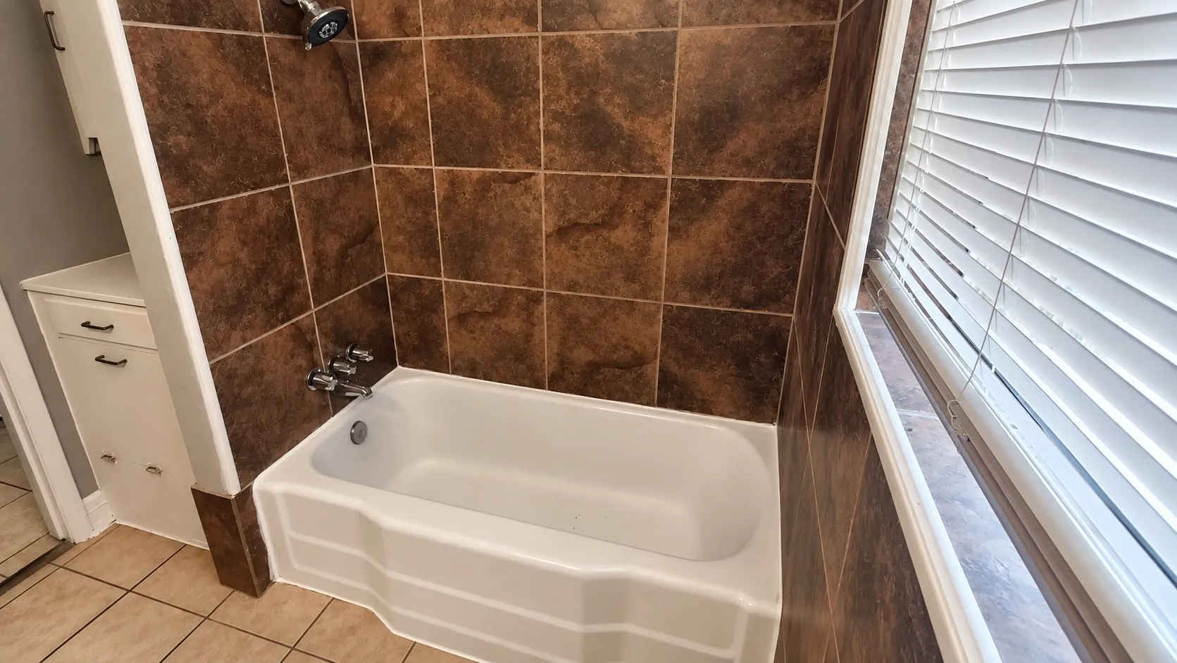 Built-in bathtub with shower head, surrounded by brown tile