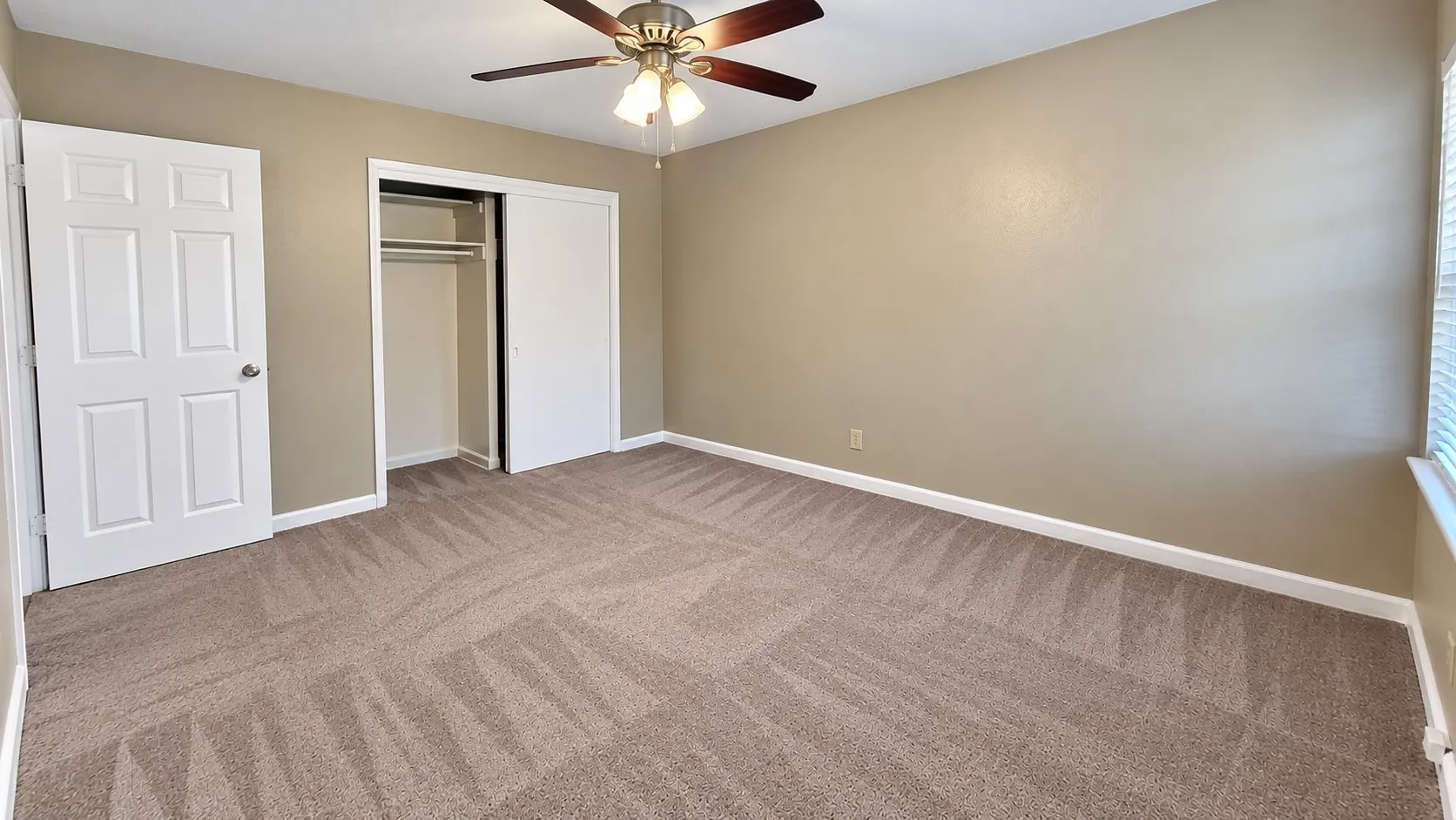 Neutral-toned walls, patterned carpet, white trim, and a ceiling fan with integrated lighting