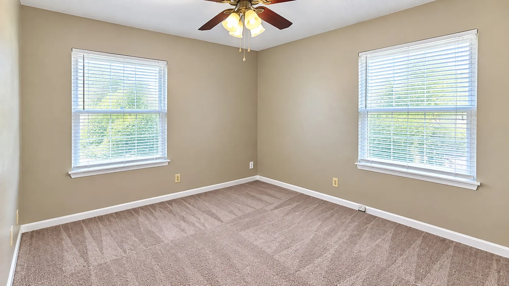 Neutral wall paint, two windows with blinds, ceiling fan with light fixture, and patterned carpet flooring