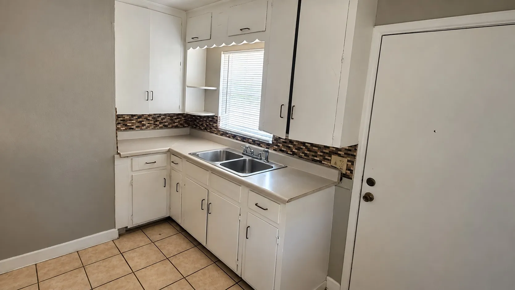 Kitchen featuring white cabinetry, a double basin stainless steel sink, a mosaic tile backsplash, and light-toned tile flooring