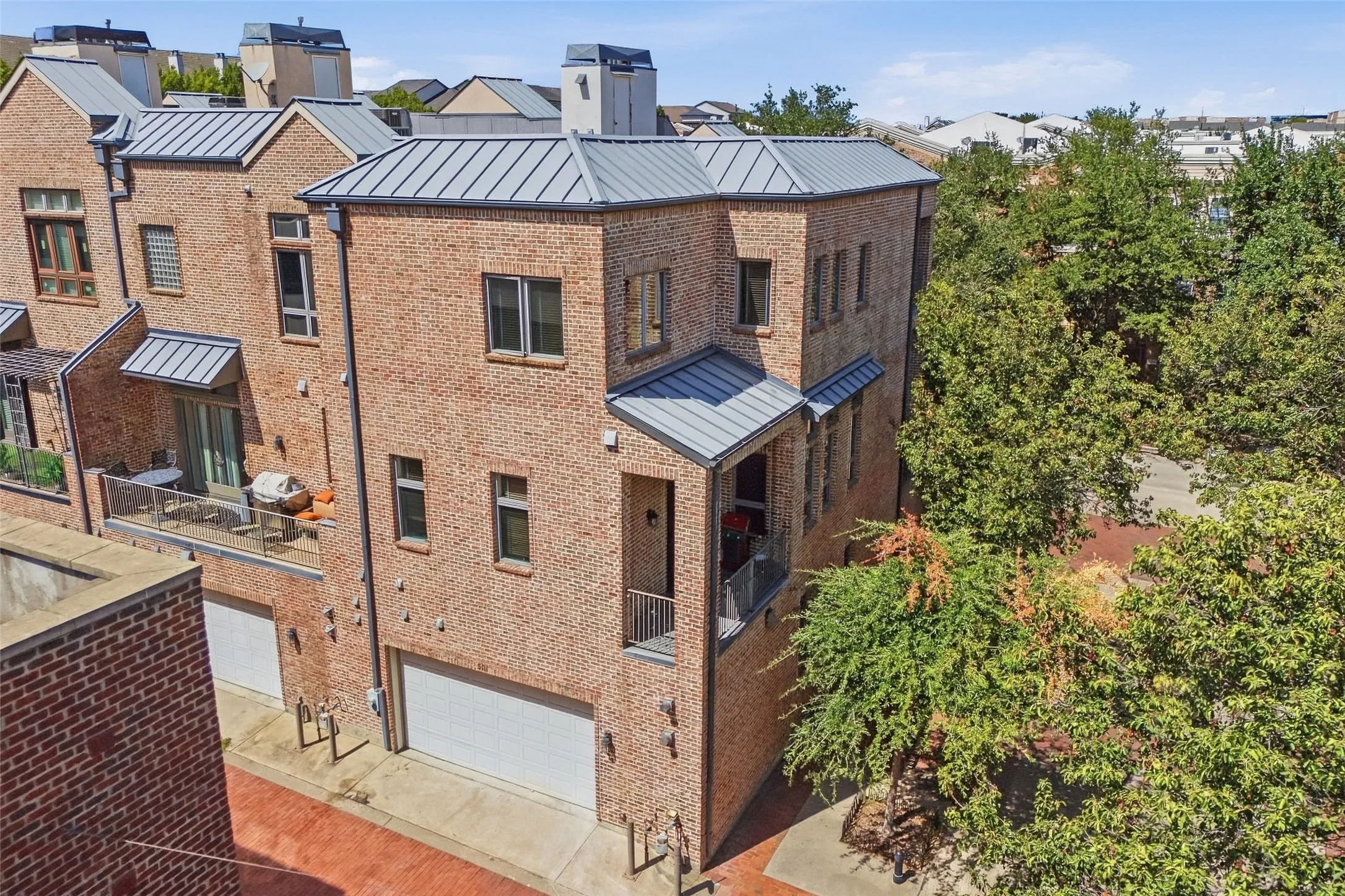 Three levels of brick under a standing-seam roof, with two balconies and the garage behind