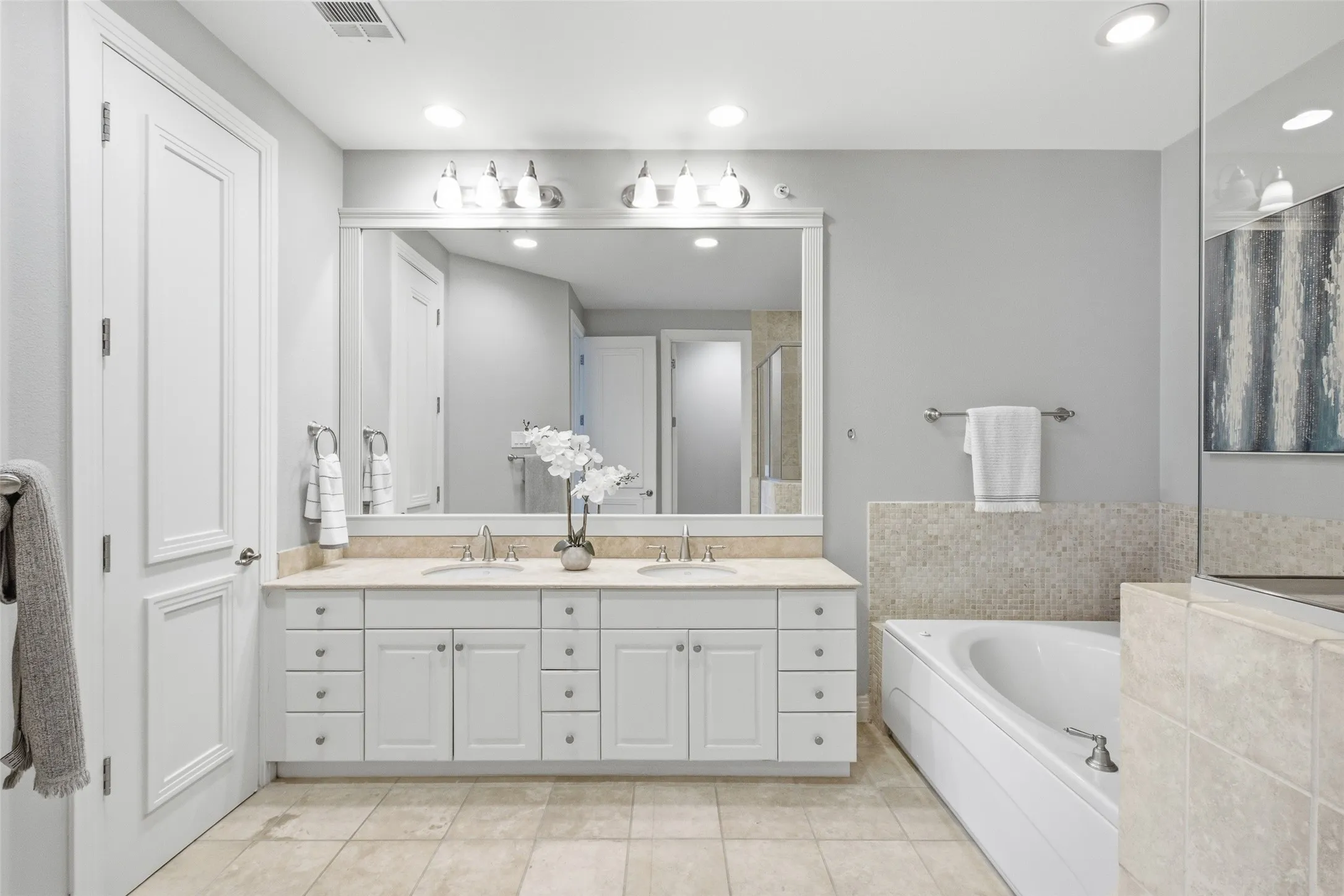 Dual sinks, a framed mirror wall, and travertine floors in the primary bath