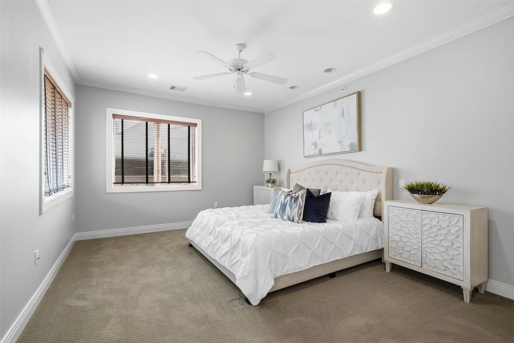 An oversized 18x23 primary bedroom with plush carpet, crown molding, and a ceiling fan