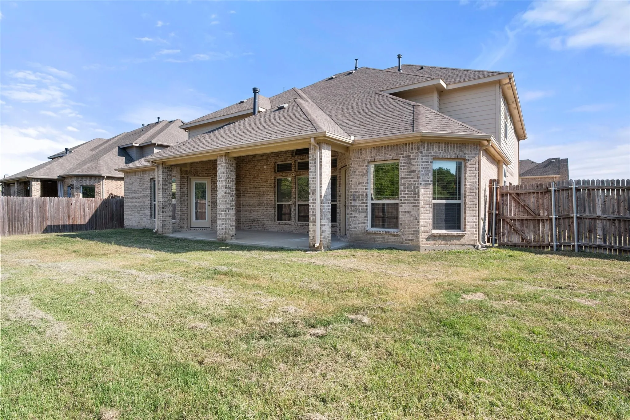 Brick exterior with a covered patio, multiple windows, and a wood privacy fence