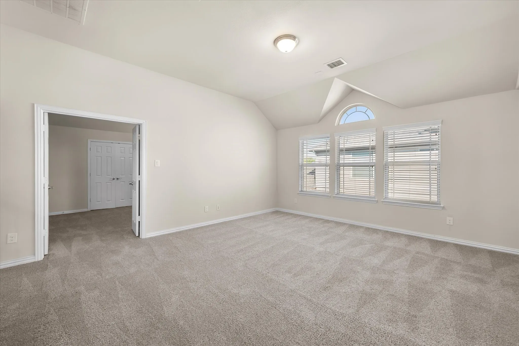Spacious room with vaulted ceilings, neutral-toned carpeting, multiple windows including an arched transom, and a flush mount ceiling light