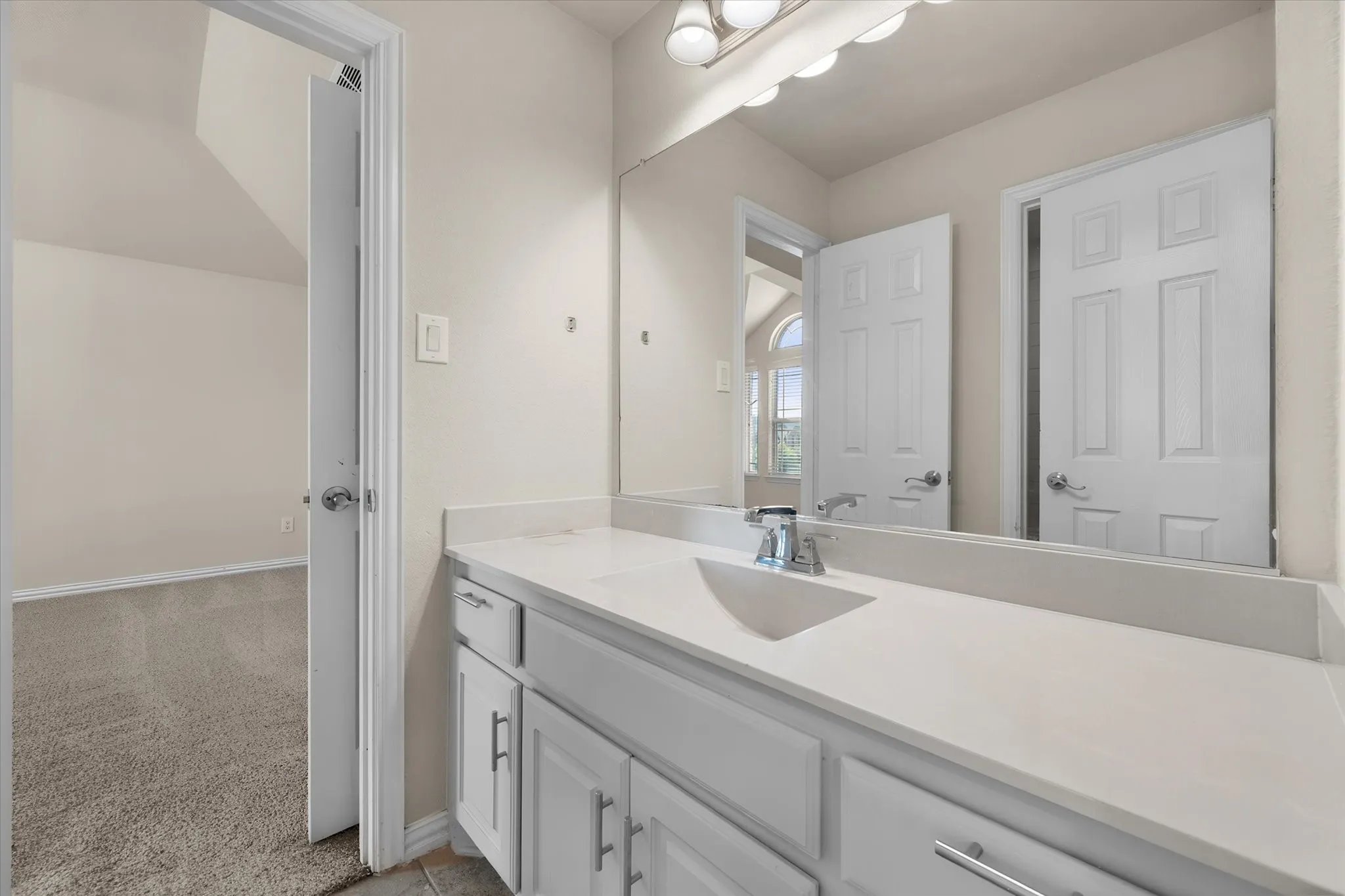 Vanity with integrated sink, chrome faucet, white cabinetry, and wall-mounted mirror
