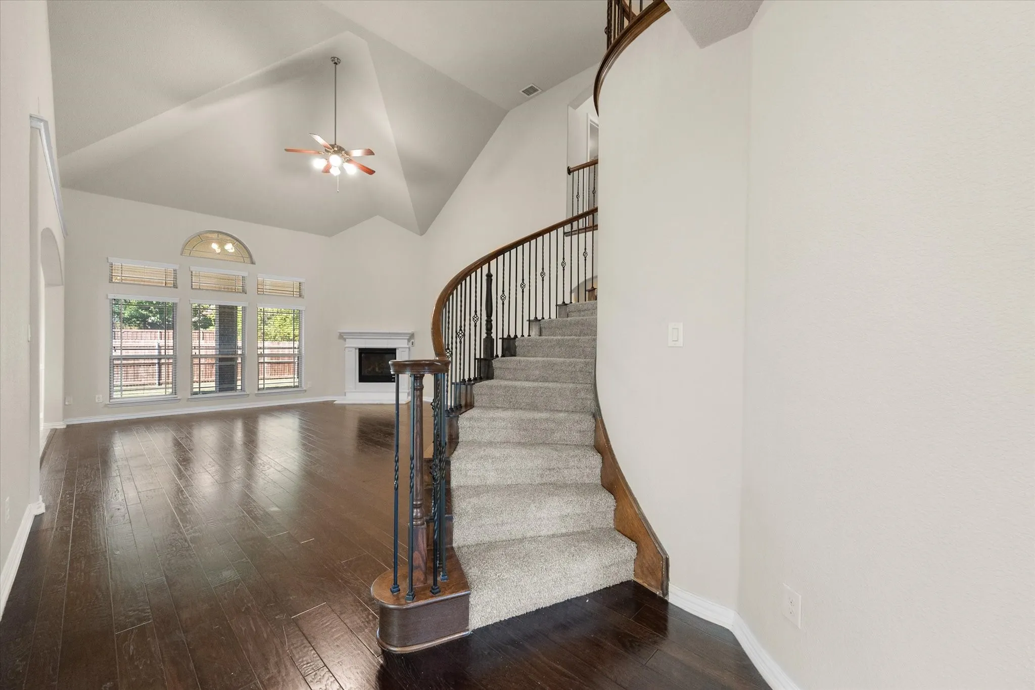 Vaulted ceilings with a ceiling fan, dark wood-finish flooring, and a fireplace with a mantel