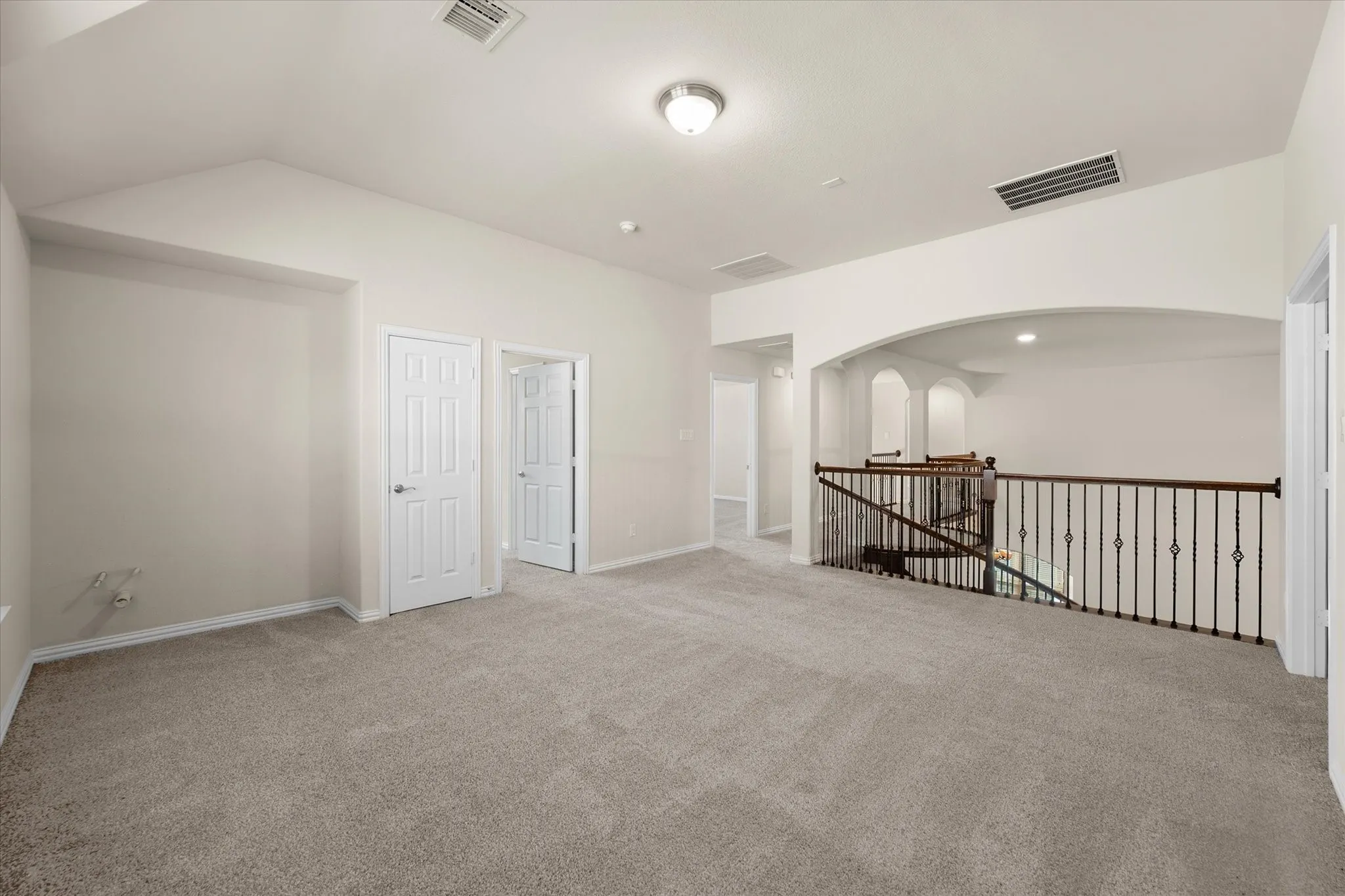 Carpeted open area featuring a vaulted ceiling and a wrought iron and wood railing