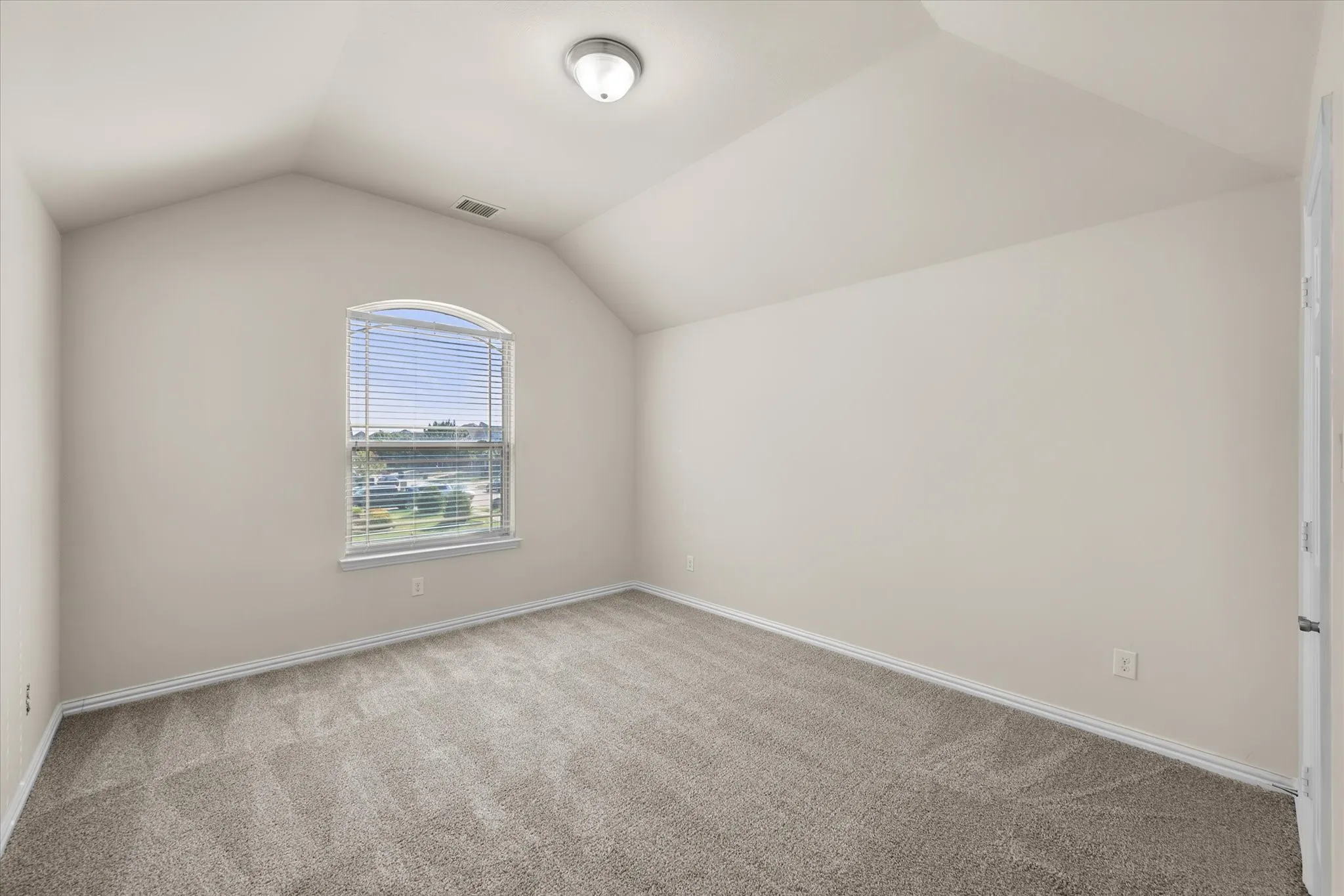 Arched window with blinds, vaulted ceiling, neutral wall tones, flush mount lighting, and carpet flooring