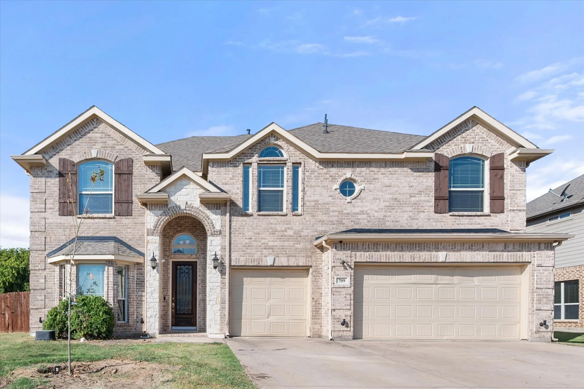 Two-story brick facade residence featuring a two-car garage, arched entry, decorative window shutters, and a bay window