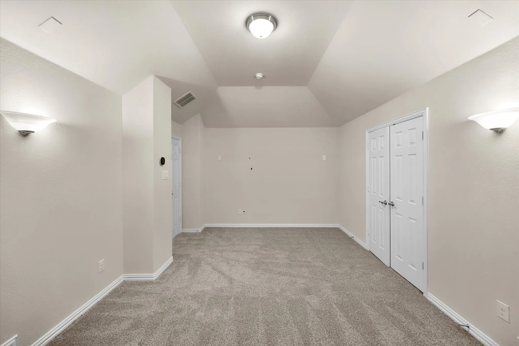 Vaulted ceiling with an overhead light fixture, carpeted flooring, and wall-mounted sconces