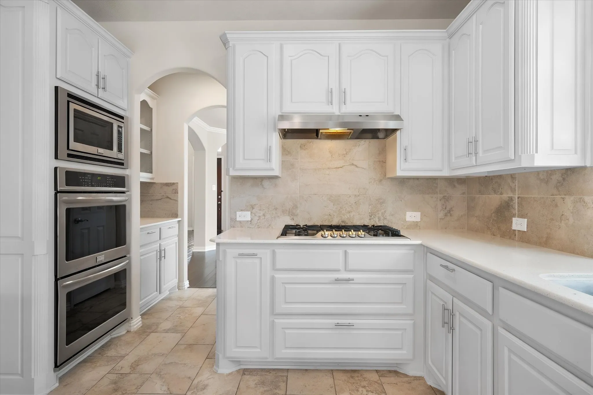 Kitchen featuring white cabinetry, light-toned tile flooring, light-toned countertops, and a gas cooktop with a stainless steel range hood