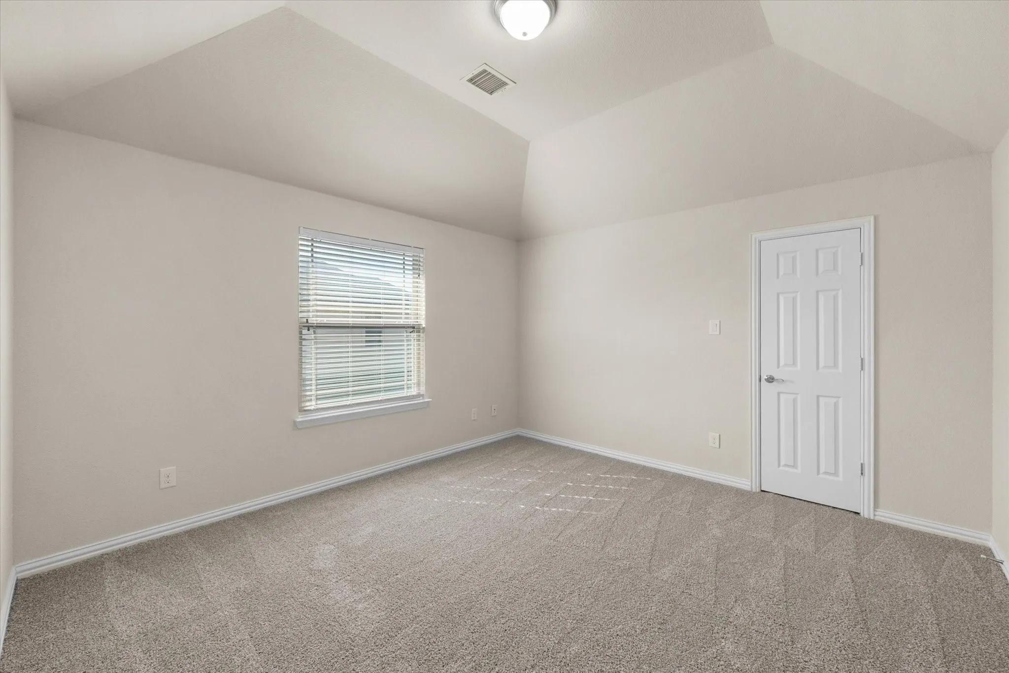 Vaulted ceiling, neutral wall tones, window with blinds, carpet flooring, and a paneled door