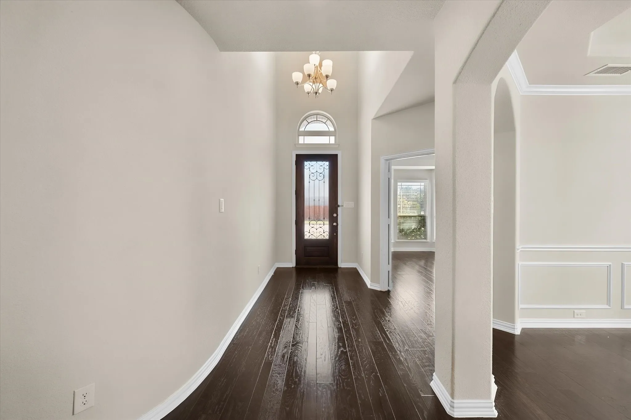 Entryway featuring wood-finish flooring, a decorative glass front door with an arched transom, a chandelier, and arched doorways