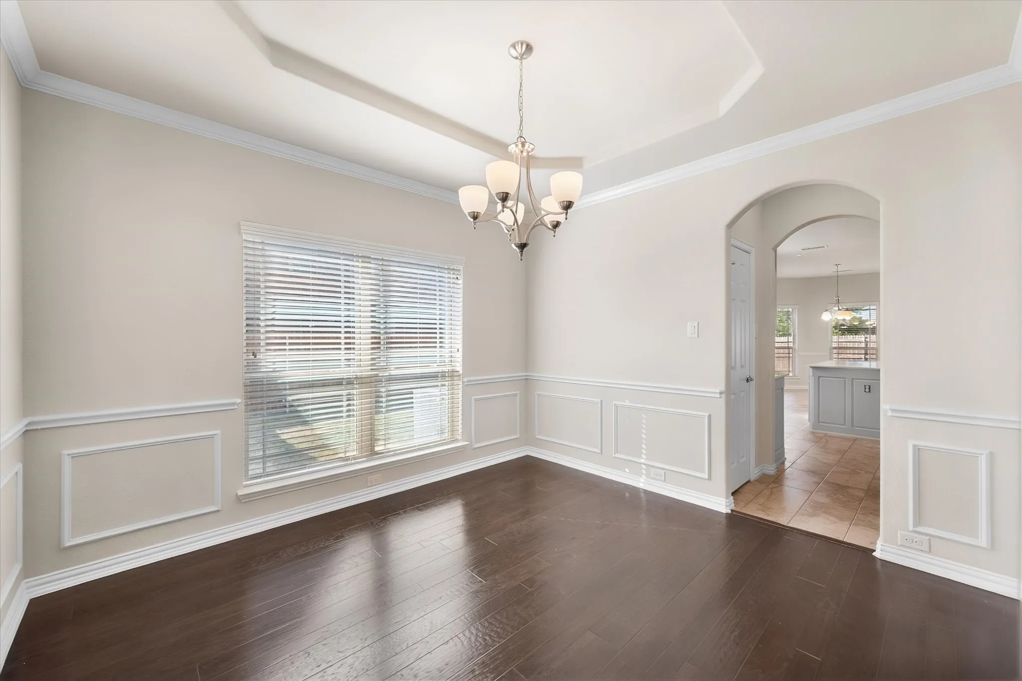 Tray ceiling with a decorative chandelier, crown molding, and wainscoting