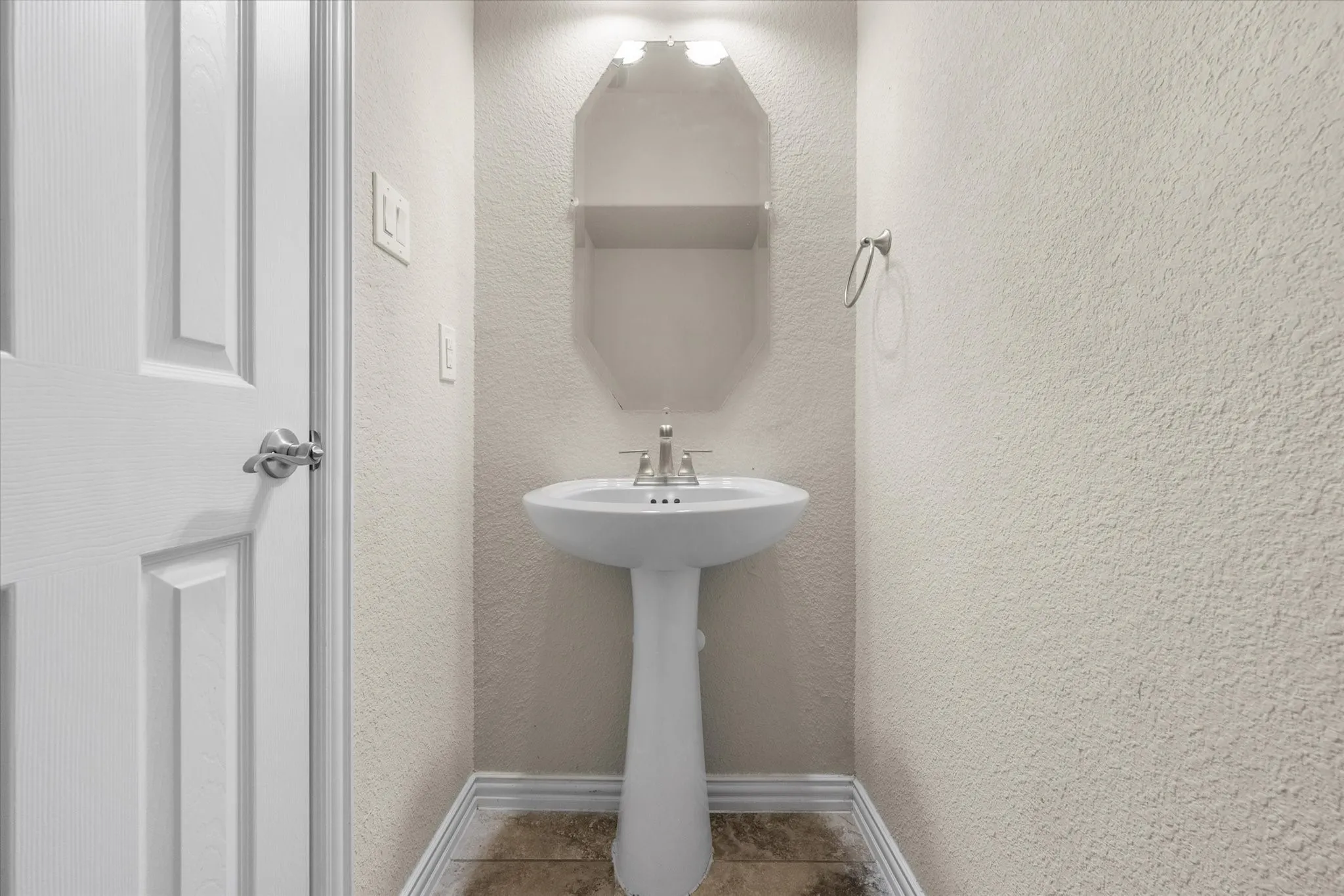 Pedestal sink with chrome faucet, textured walls, overhead lighting, and wood-finish flooring