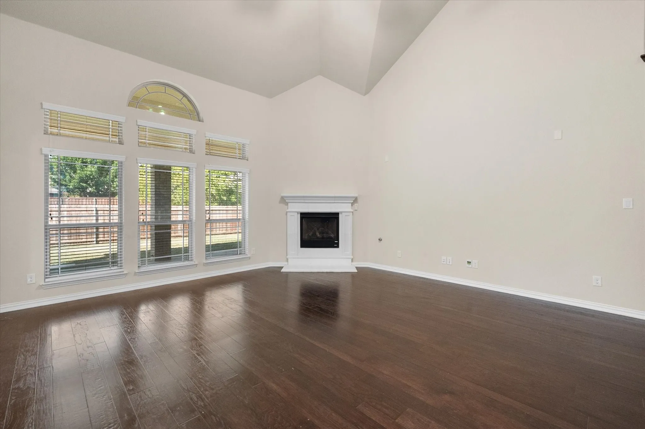 Vaulted ceiling, wood-finish flooring, white fireplace with mantle, multiple windows, and arched transom window