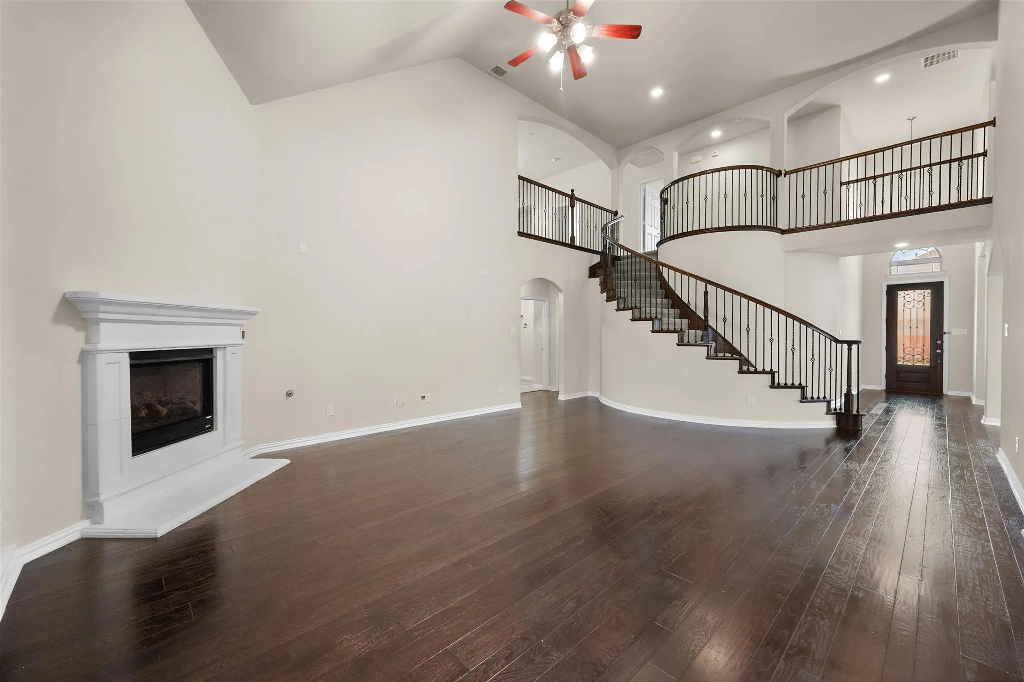 Spacious living area featuring a fireplace with a white mantel, high vaulted ceilings, and dark wood-finish flooring