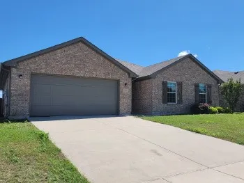 Brick exterior with an attached two-car garage, concrete driveway, and established landscaping