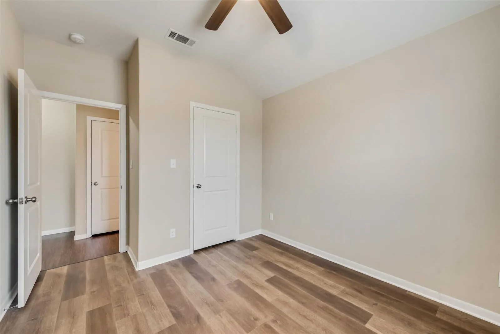 Vaulted ceiling, wood-finish flooring, ceiling fan, neutral wall paint, white interior doors