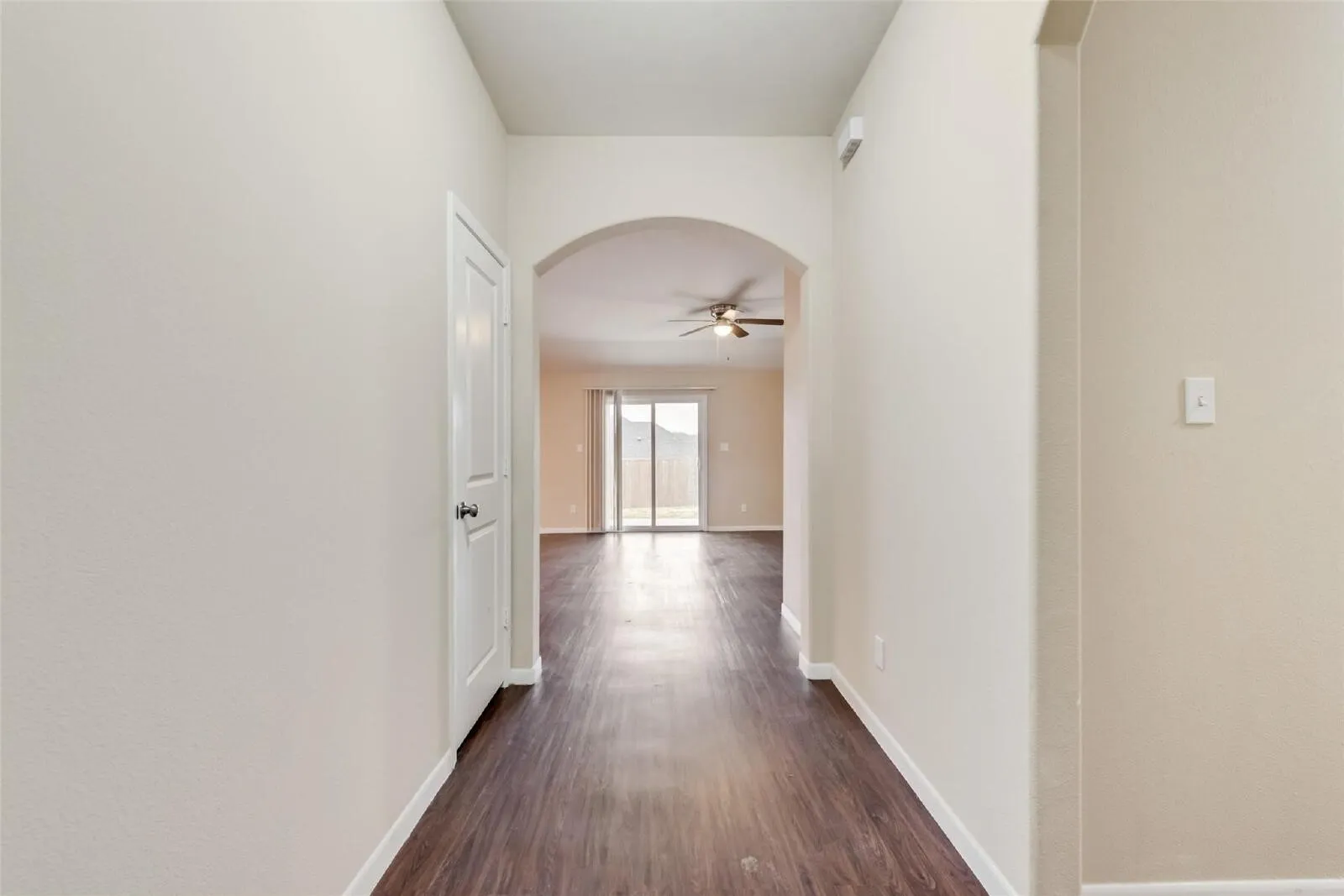 Archway entry to living area featuring wood-finish flooring, ceiling fan, and sliding glass doors