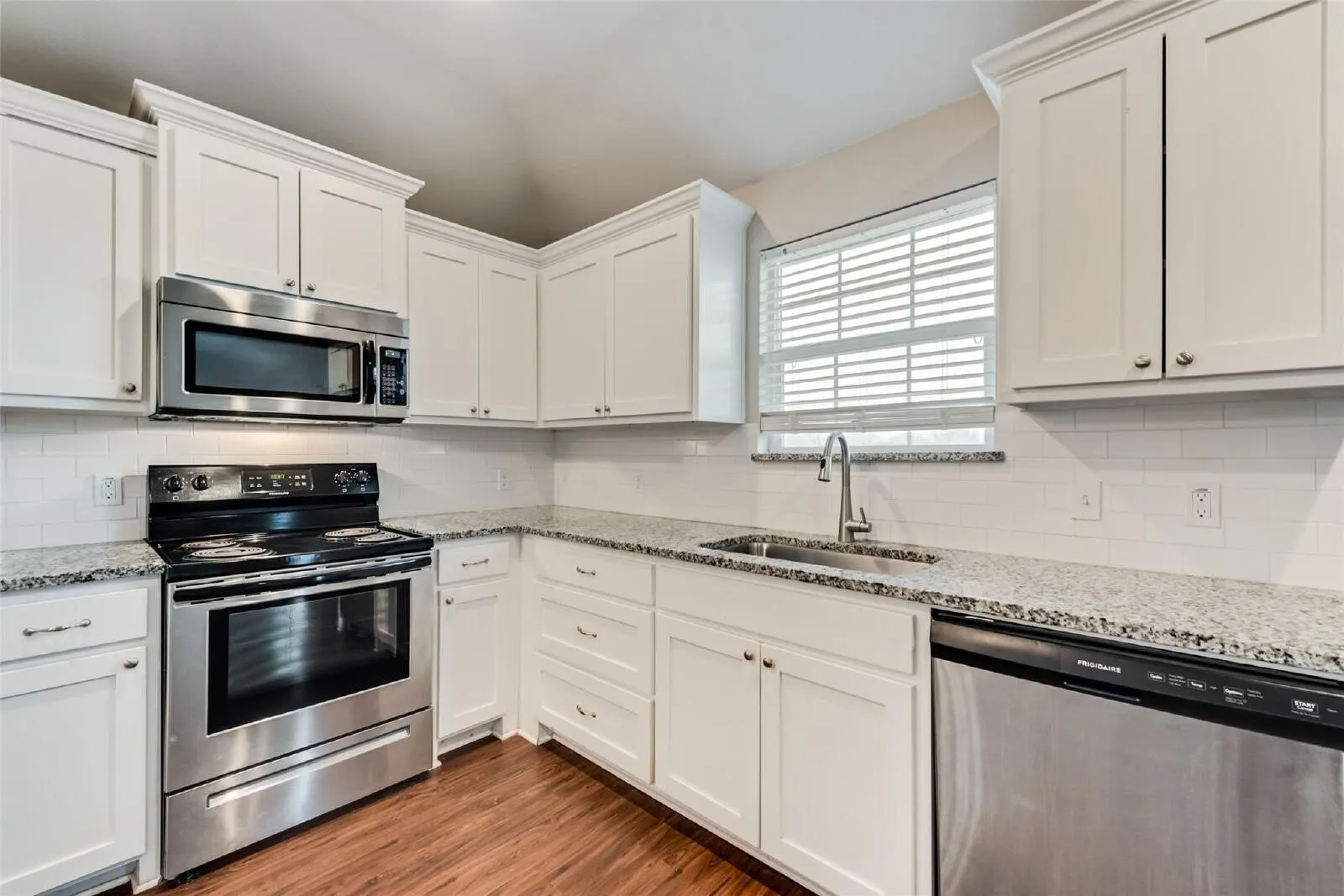 Kitchen featuring white shaker-style cabinetry, stainless steel appliances, speckled stone countertops, and a subway tile backsplash
