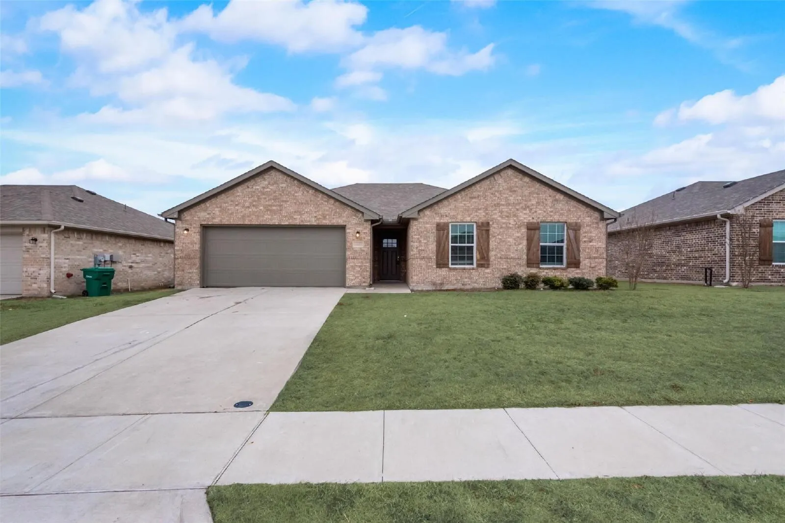 Brick exterior with wood-tone shutters, attached garage, concrete driveway, and a front lawn
