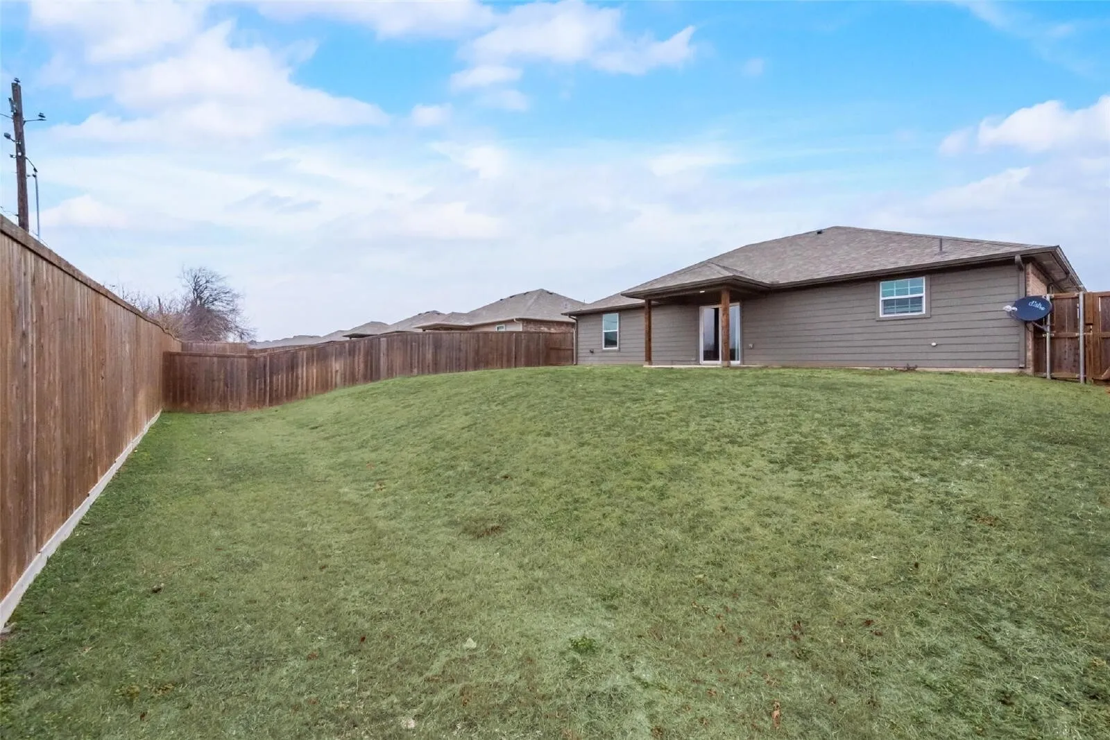 Expansive backyard featuring a manicured lawn, wood privacy fencing, and a covered patio with wood columns