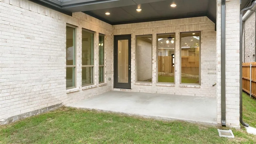 Covered concrete patio with recessed lighting, brick exterior, and multiple tall windows