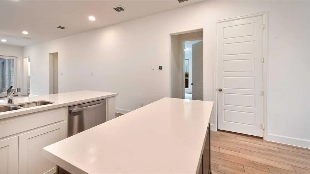 Kitchen featuring two islands with light-toned countertops, a stainless steel double basin sink with a gooseneck faucet, white shaker-style cabinetry, and a built-in stainless steel dishwasher
