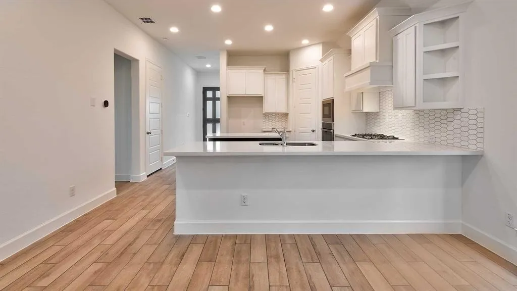 Wood-finish flooring throughout, white shaker-style cabinetry, white countertops, built-in microwave, and a gas range