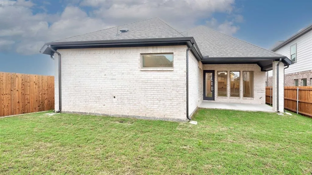 White brick exterior with a covered patio, dark roofing, and a wooden privacy fence