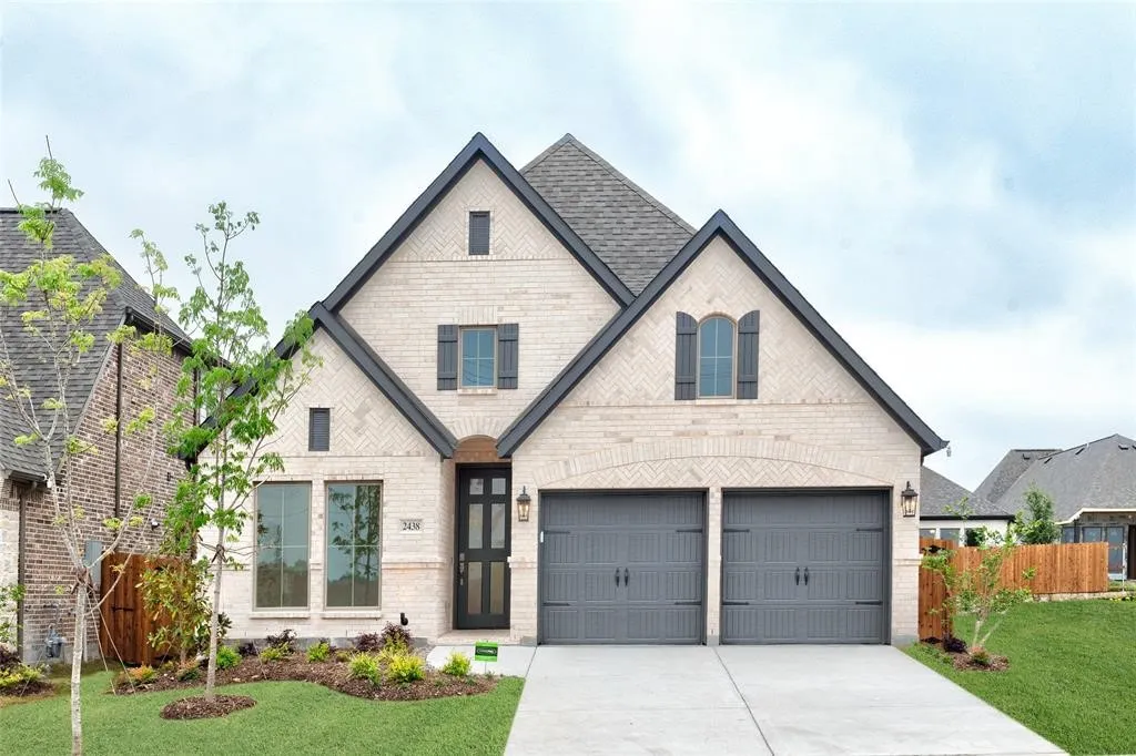 Brick facade with dark trim accents, arched entry, two-car garage, and landscaped front yard with mature trees
